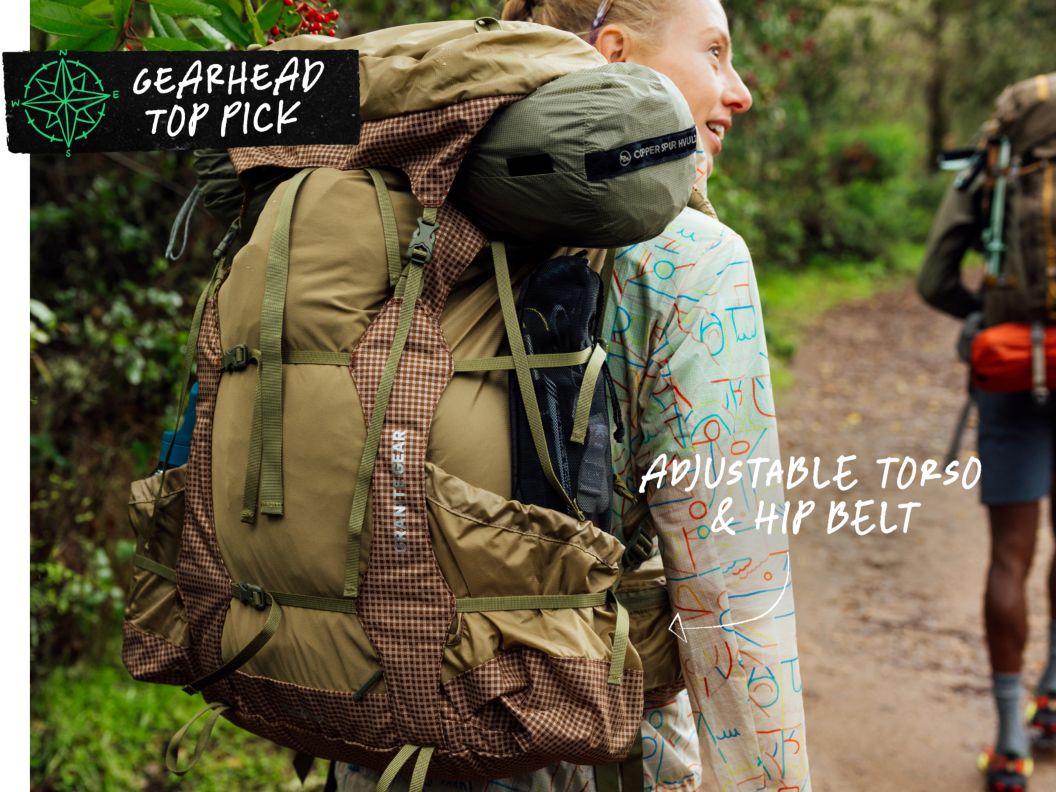 A woman wears a fully loaded brown backpacking pack. Text overlay reads: Gearhead Top Pick, adjustable torso & hip belt.